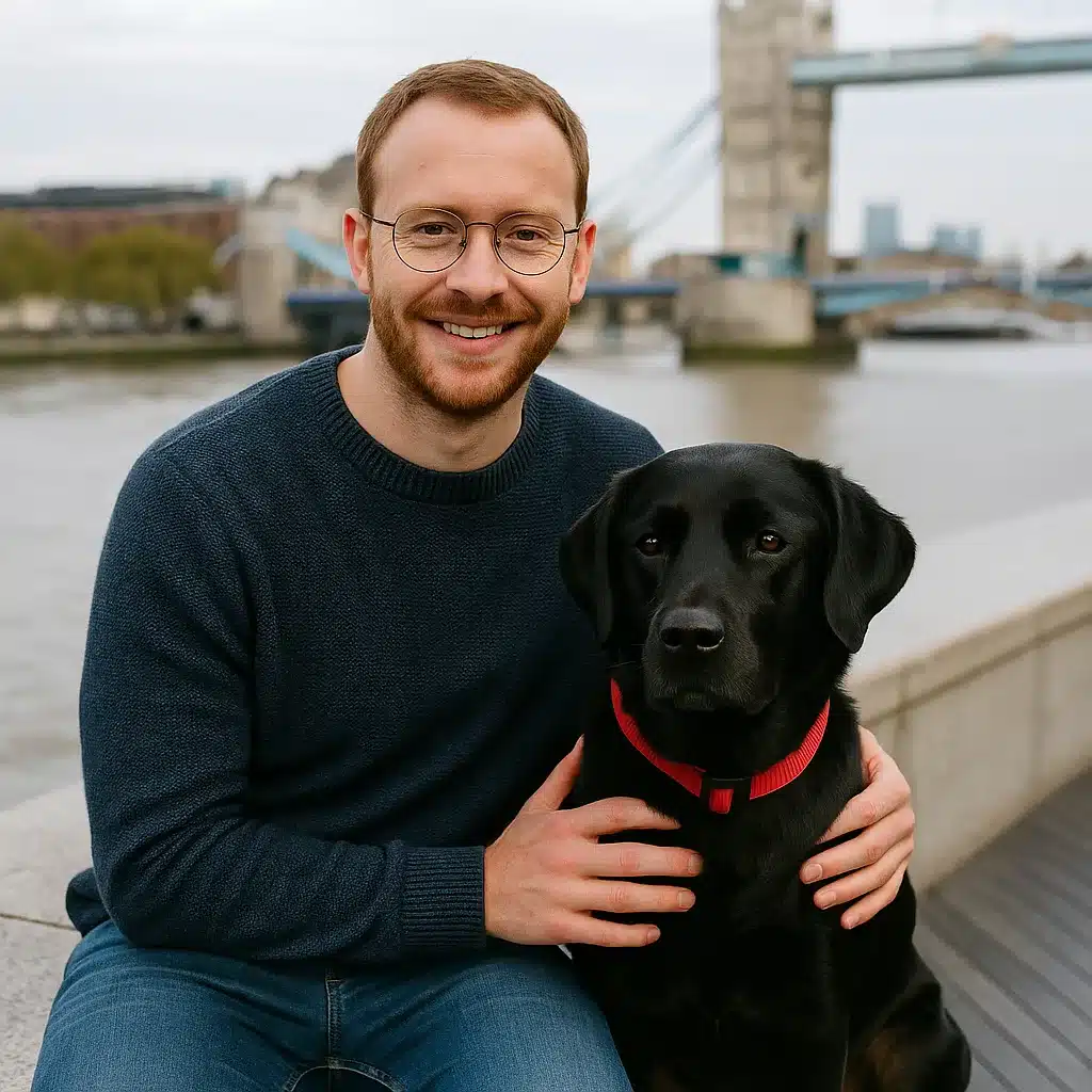 Man sitting by the river with his black Labrador Retriever near Tower Bridge in London